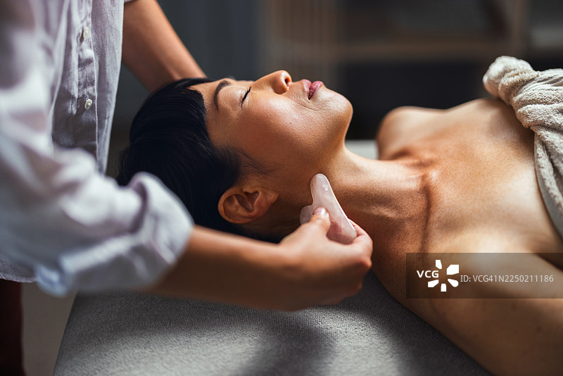 使用玉石工具在颈部和下颌线进行放松的美容面部按摩图片素材