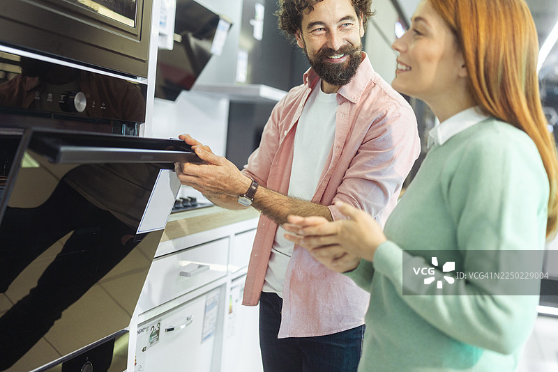无忧无虑的恩爱夫妻在黑色星期五购物季，对高端厨房电器的深度折扣感到非常兴奋。他们正在仔细查看烤箱或炉灶的功能。图片素材