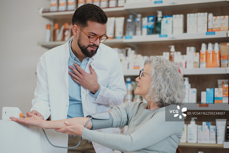 药剂师在药店为一位老年女性测量血压图片素材
