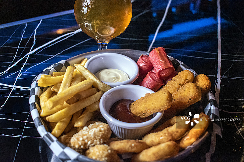 炸薯条、香肠、马苏里拉奶酪条、炸鸡和洋葱圈拼盘。一杯精酿啤酒。美食。快餐。图片素材