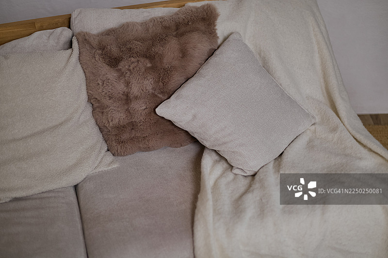 一个浅色沙发上摆放着一堆毛绒靠垫和一条毯子。图片素材