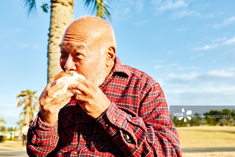 一位老人正在阳光明媚的早晨在草坪户外享用早餐。图片素材