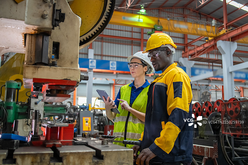 工业工人在生产线上检查机器并讨论工作流程。现代制造业中的专业团队合作、安全和精准。图片素材