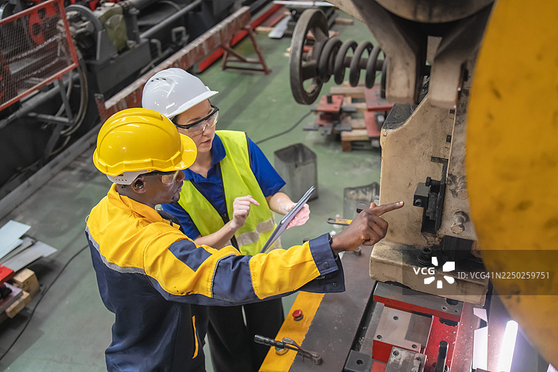 工业工人在生产线上检查机器并讨论工作流程。现代制造业中的专业团队合作、安全和精准。图片素材