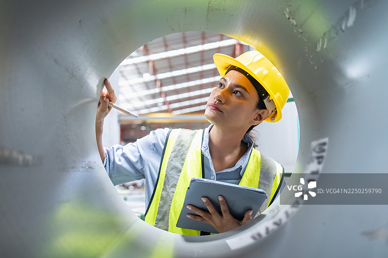 女性产业工人正在生产线上工作，专注于实际的工程操作，进行精细的金属板检查工作。图片素材