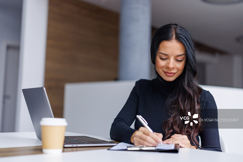 一位专业的女性在办公桌前写笔记，记录工作进展图片素材