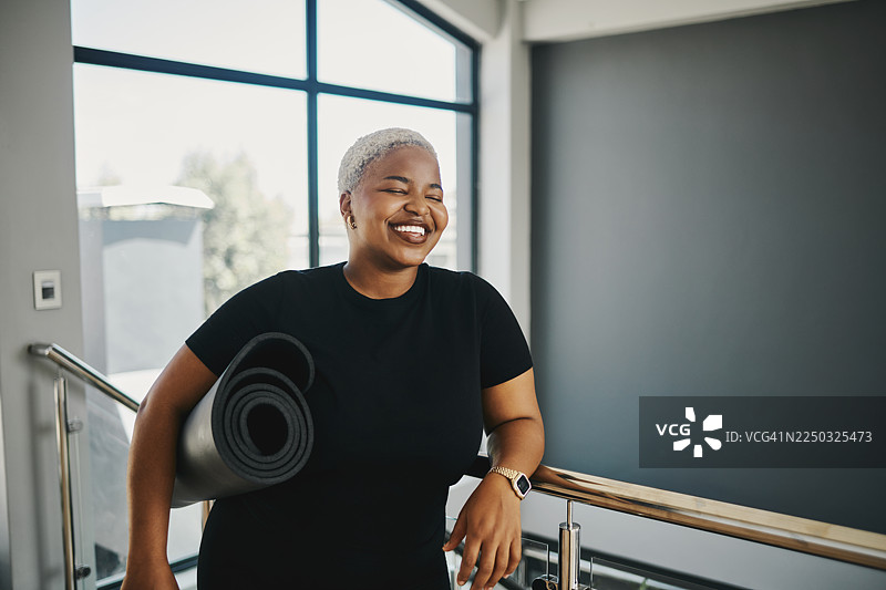 年轻的微笑女子在室内健身后，带着瑜伽垫休息图片素材