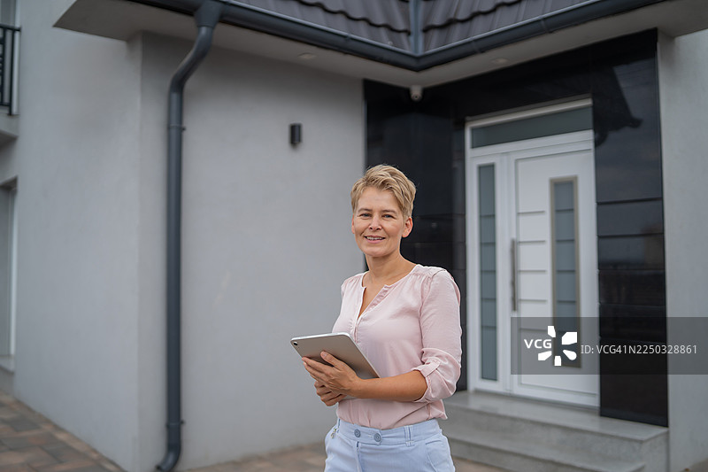 女房地产估价师手持平板电脑站在房屋前图片素材