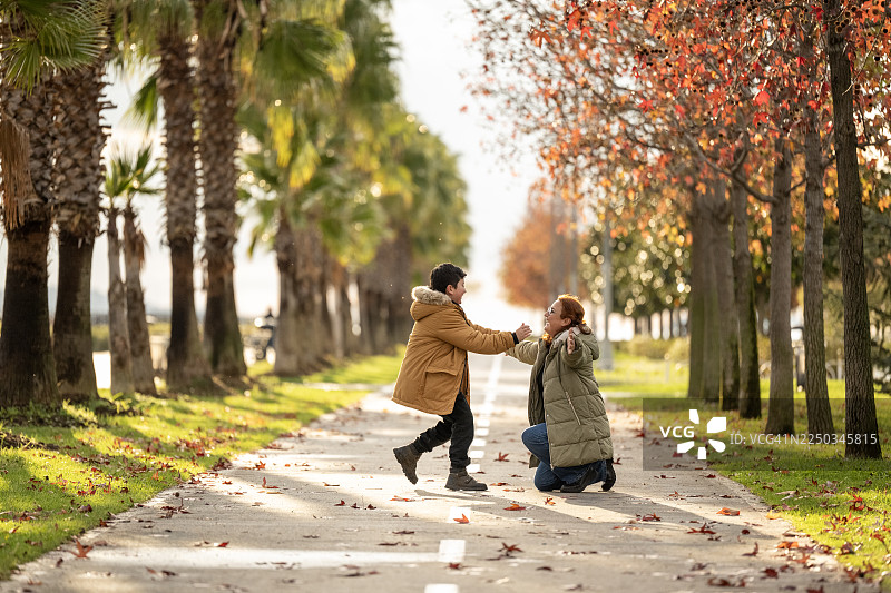 一个孩子跑进城市公园，跳进他母亲的怀抱并拥抱她。一系列照片的一部分图片素材