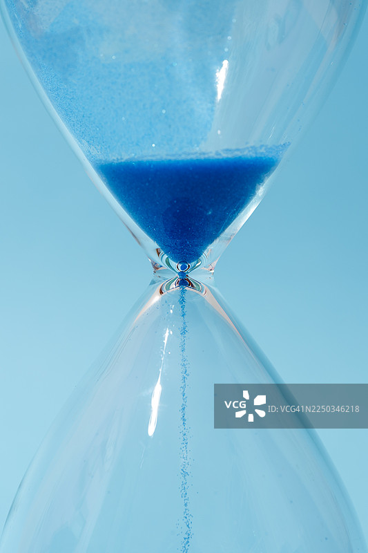 蓝色沙子在沙漏中流淌，计量着时间图片素材