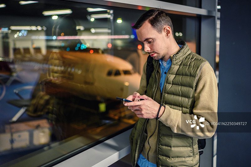 年轻男子在机场休息室里，手持手机等待登机图片素材
