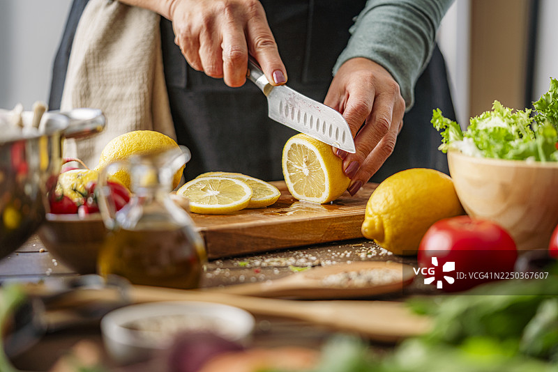 一位看不清面容的女性正在切新鲜采摘的有机柠檬。多汁健康的果实，富含维生素，有益身心健康，适合在家准备素食。图片素材