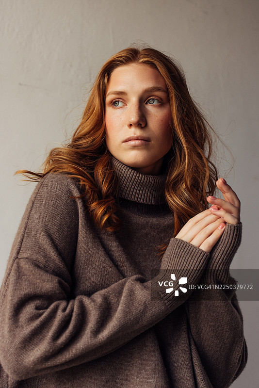 一位留着红发、身穿舒适棕色高领毛衣的年轻女性的肖像，表情若有所思图片素材