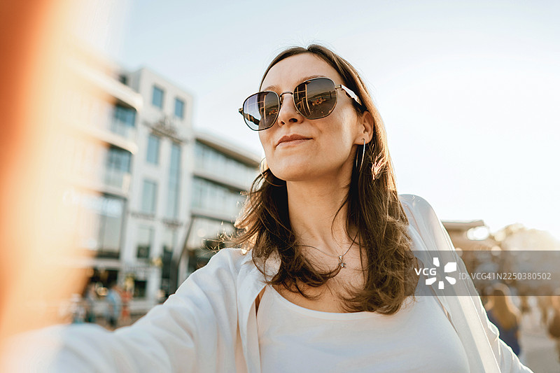 戴着太阳镜、面带笑容的女子在户外自拍图片素材