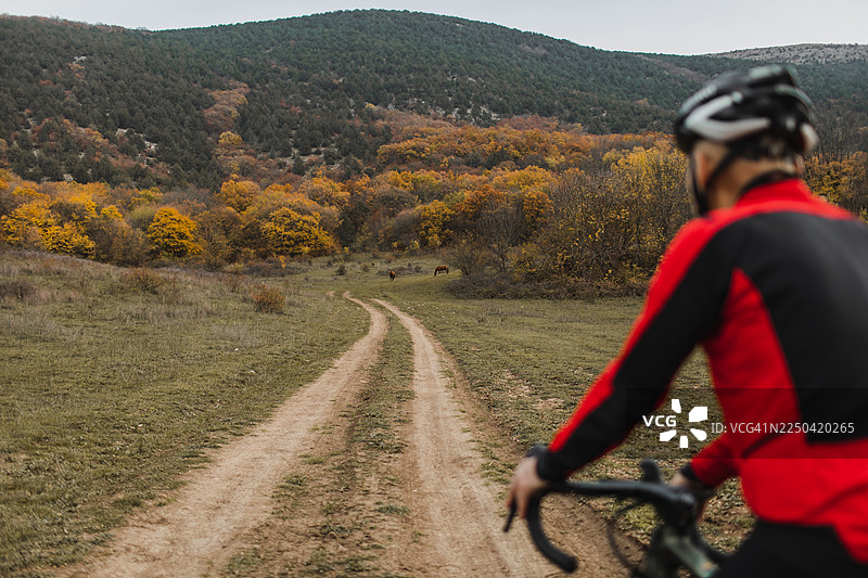 秋季砂石骑行：骑行者在前景，穿过色彩斑斓的山丘，在泥土小径上骑行图片素材