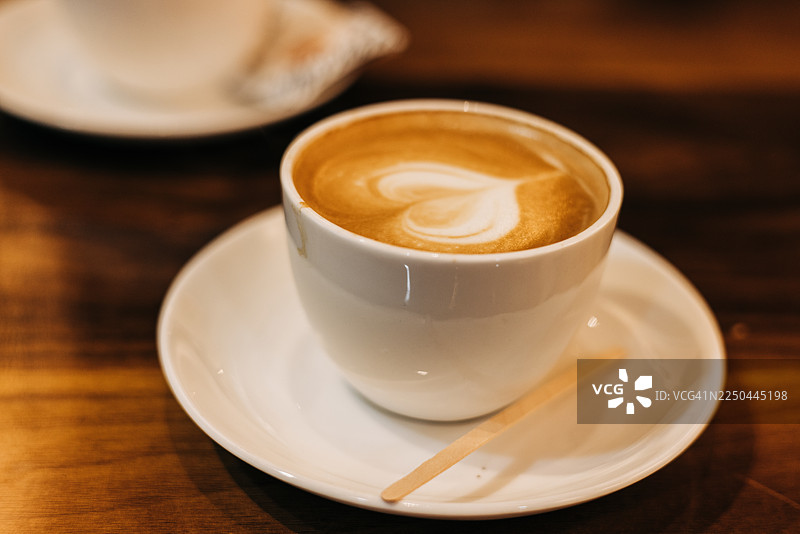 木制咖啡馆桌上的新鲜卡布奇诺咖啡，上面有心形拿铁拉花图片素材