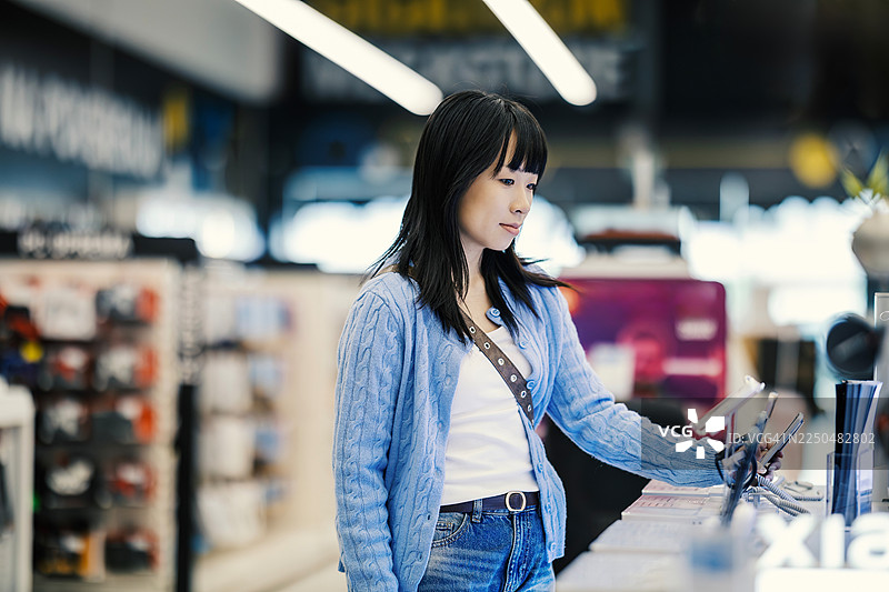 亚洲女性在电子产品商店选购智能手机图片素材