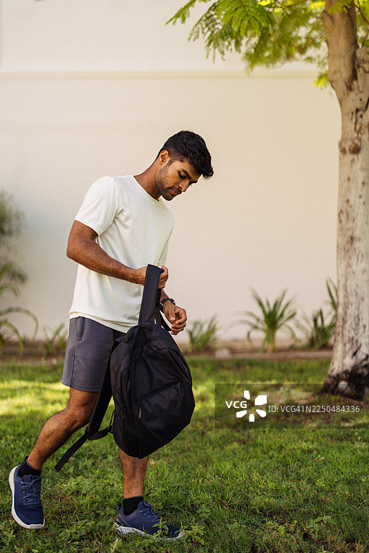 年轻男子背着背包，在阳光明媚的公园里准备出发图片素材
