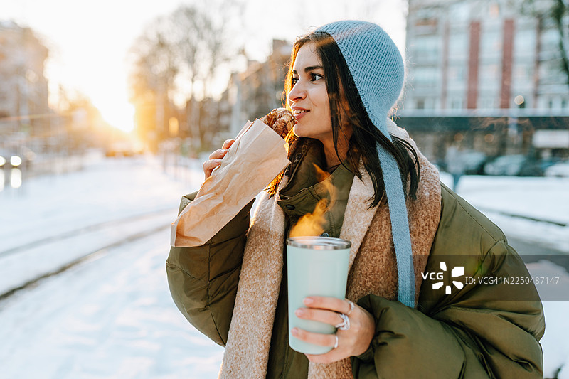 年轻女子在冬日城市中享用热乎乎的糕点和热饮图片素材