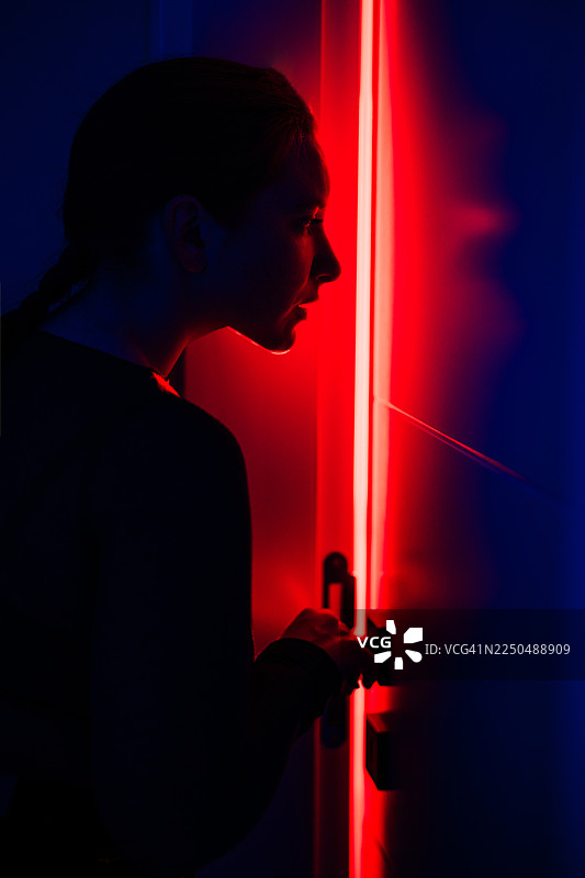 黑暗房间的门框中透出红色的垂直光线，映照出一女子剪影。图片素材