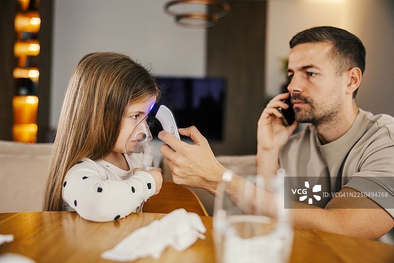 父亲在家中帮助孩子使用雾化器并测量体温图片素材