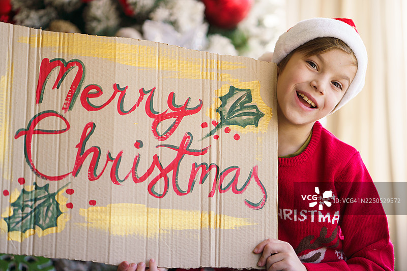 快乐的孩子举着圣诞快乐的纸板标志。图片素材