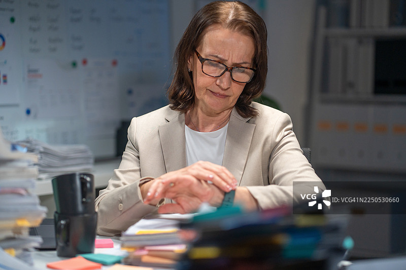 疲惫不堪的高级女商人深夜处理文件，承受着巨大压力。图片素材