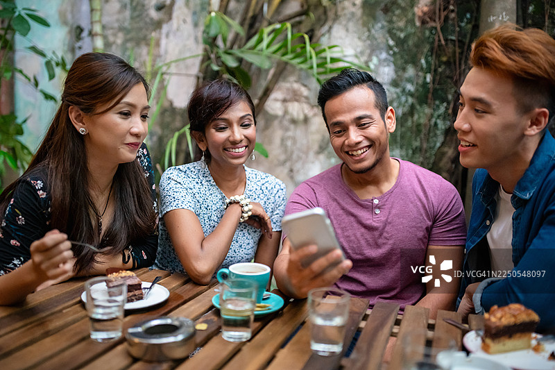 一群朋友在户外咖啡馆的桌子旁，一起笑着看智能手机图片素材