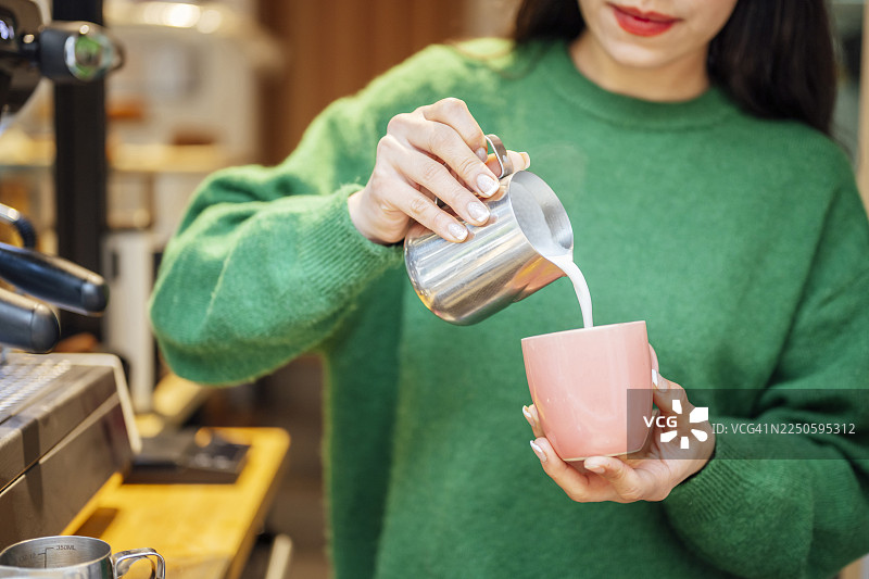 咖啡师在咖啡杯中倒入打发好的牛奶，制作拉花艺术图片素材