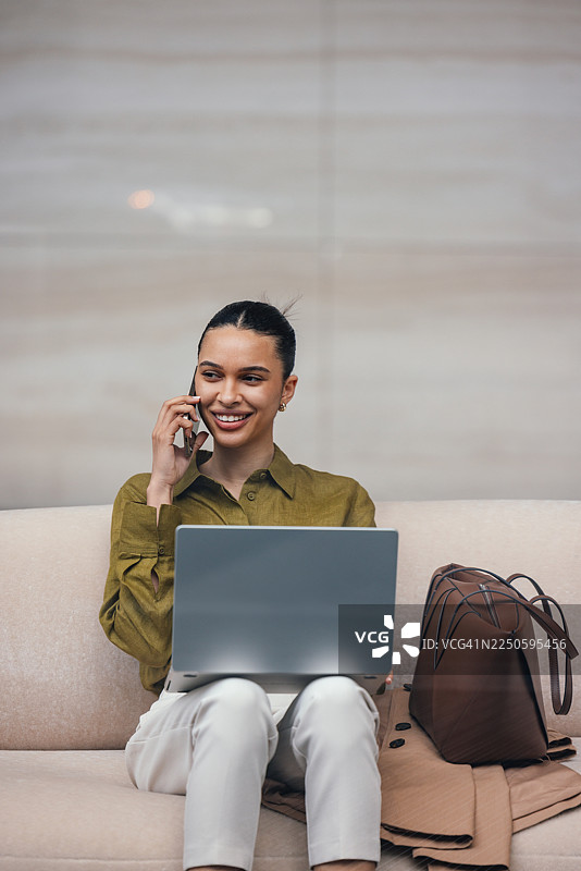一位女商人坐在现代办公室休息室的笔记本电脑前，边打电话边微笑图片素材