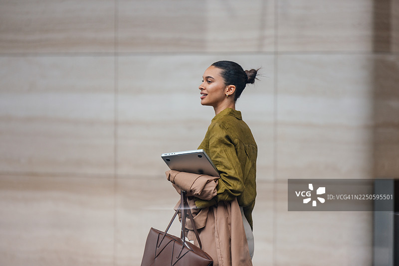 职业女性在城市街景中，手持平板电脑和手提包外出行走图片素材
