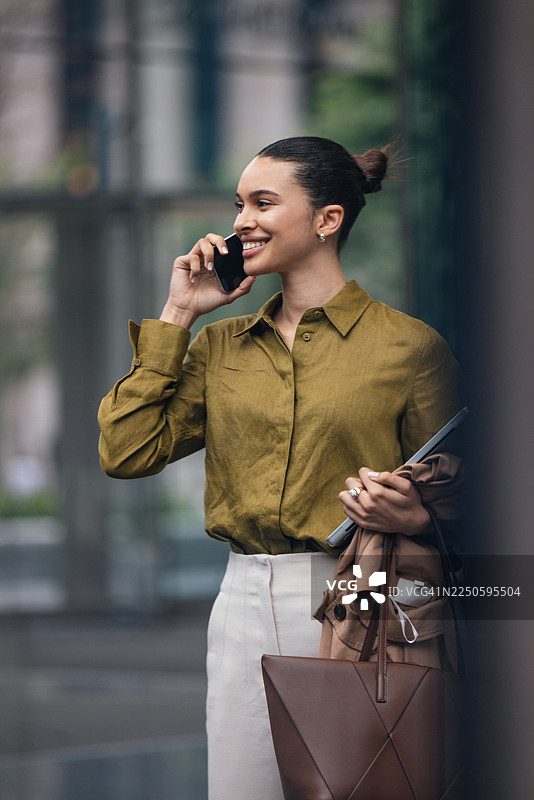 职业女性在城市街道上，一手拿着笔记本电脑和购物袋，一手接听电话图片素材