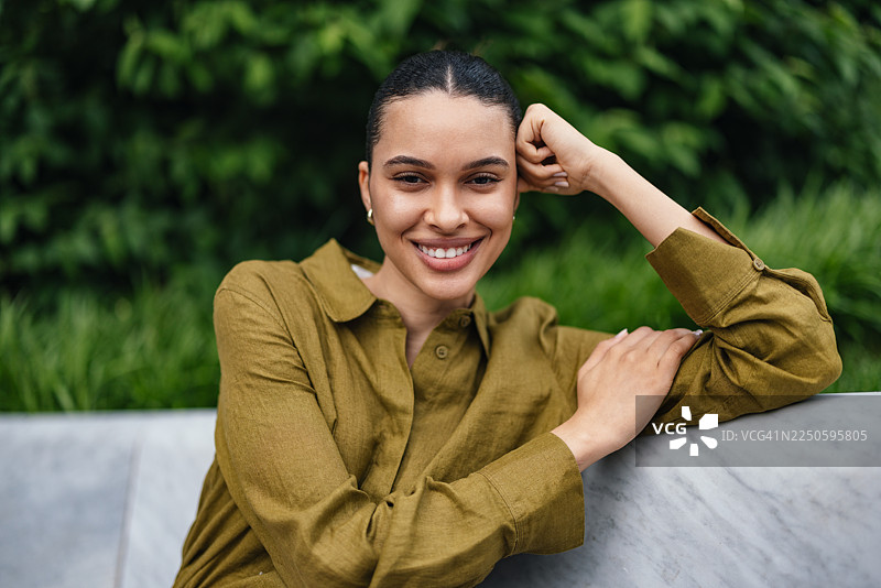 自信的商界女性在户外大理石栏杆旁放松肖像，身处绿色公园，今日展露笑容，自然状态图片素材