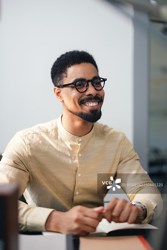 身处现代办公室中，戴眼镜的男士在办公桌旁微笑，显得专业而友好图片素材