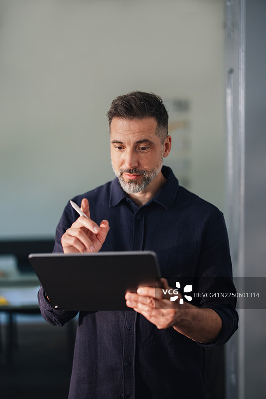 在现代办公室环境中，一名男子正专注地使用触控笔分析平板电脑，展现商务场景。图片素材