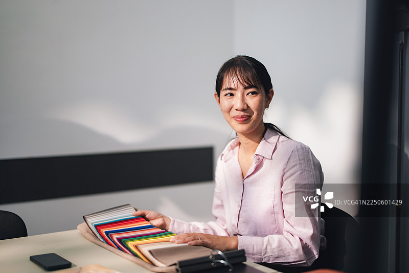 在现代办公室里，专业女性手持布料色卡，适用于设计和纺织行业图片素材