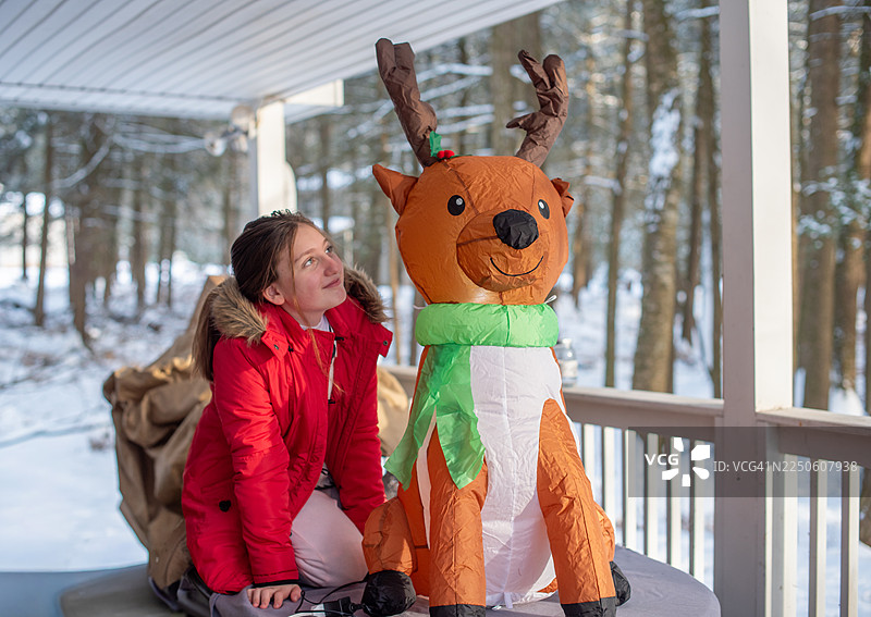 十二月下午，一名初中女生在有顶的露台上布置充气驯鹿装饰。在宾夕法尼亚州山区的家庭住宅进行节日装饰。图片素材