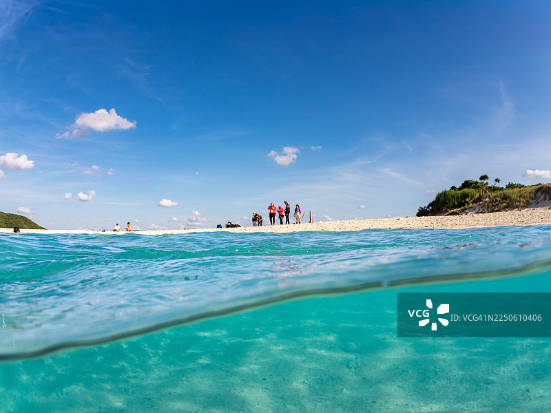 美丽的海滩，沙子是白色的。游客在海滩上浮潜。半水面拍摄。还有其他的。日本冲绳县阿嘉岛，热带鱼群。美丽的珊瑚礁和游泳的人们。座间味岛，庆良间群岛，岛尻郡，日本图片素材