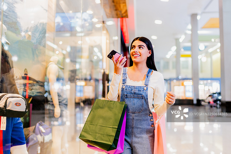 年轻女孩提着购物袋在购物中心边走边发送语音消息图片素材