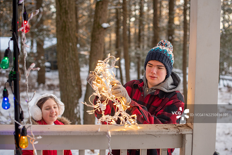 患有自闭症的哥哥和13岁的妹妹在山间小屋一起进行季节性家居装饰项目。冬季下午，户外门廊布置着温暖的串灯。图片素材