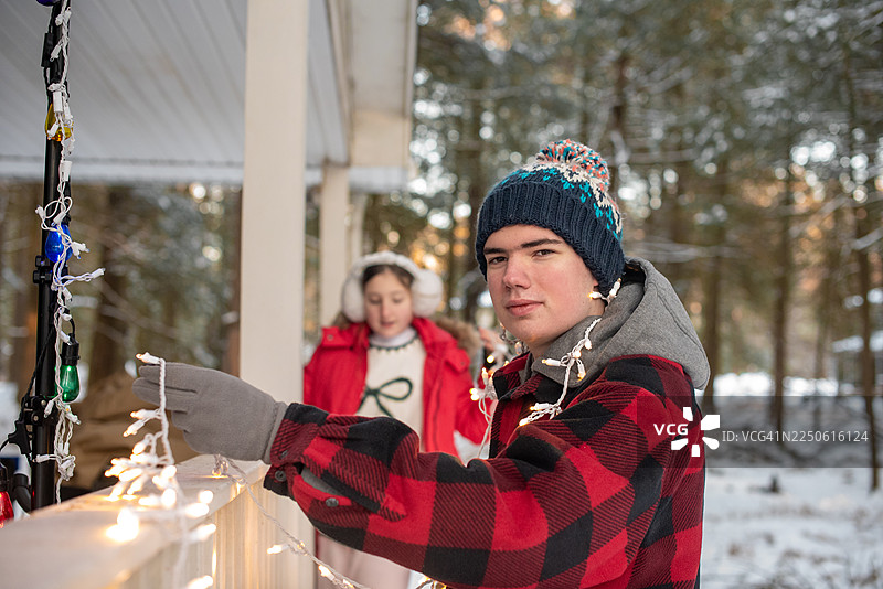 12月下午，在美国宾夕法尼亚州波科诺山，一名患有自闭症谱系障碍的年轻成年人在山间房屋门廊的栏杆上，小心翼翼地安装着节日灯饰。图片素材