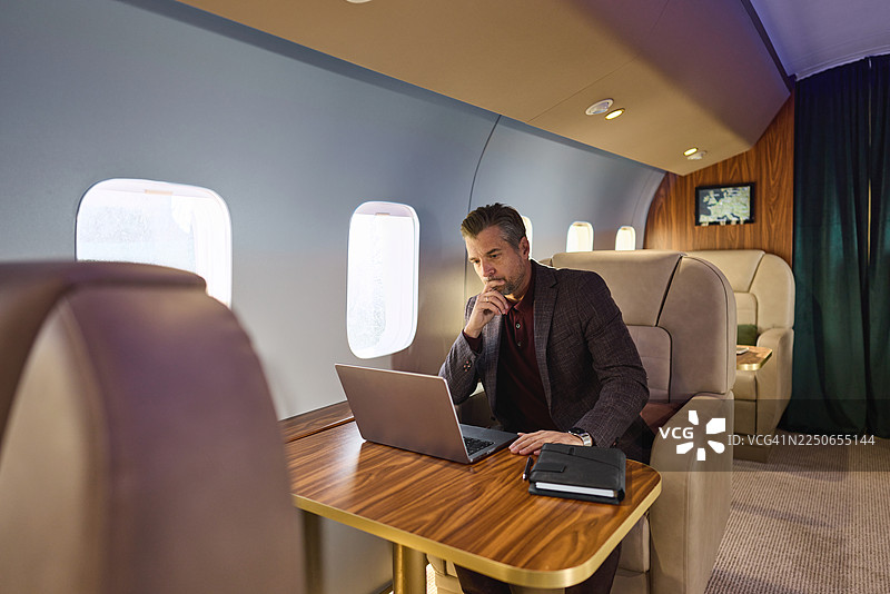 一位商业人士在私人飞机上思考着用笔记本电脑。图片素材