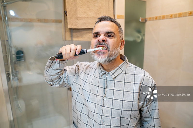 浴室里，一位成熟的男士正在用电动牙刷刷牙图片素材