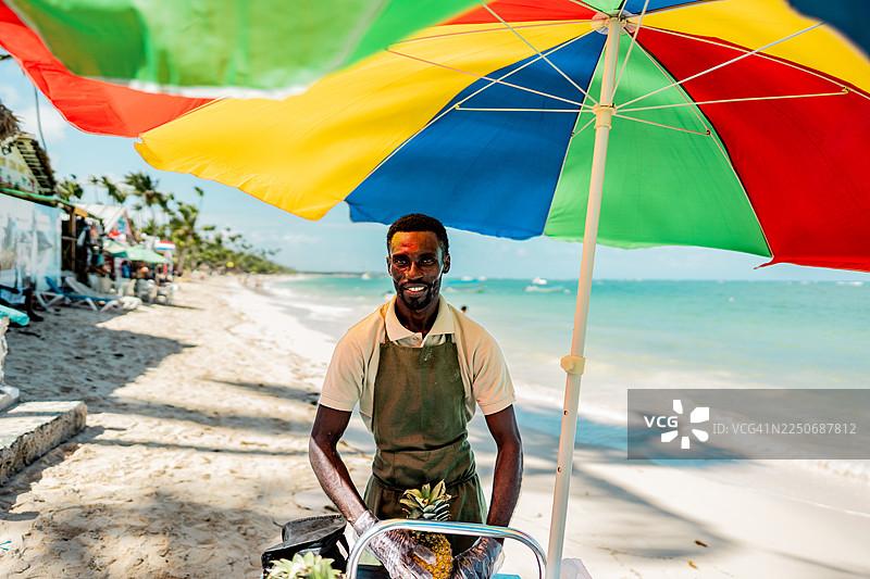 海滩上，一位中年男销售员正在售卖菠萝的肖像照图片素材