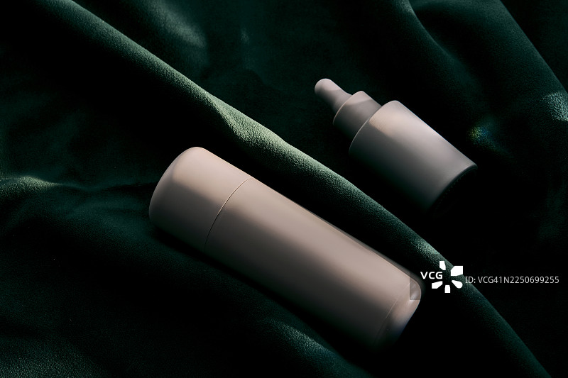 深绿色天鹅绒上的滴管瓶护肤品包装图片素材