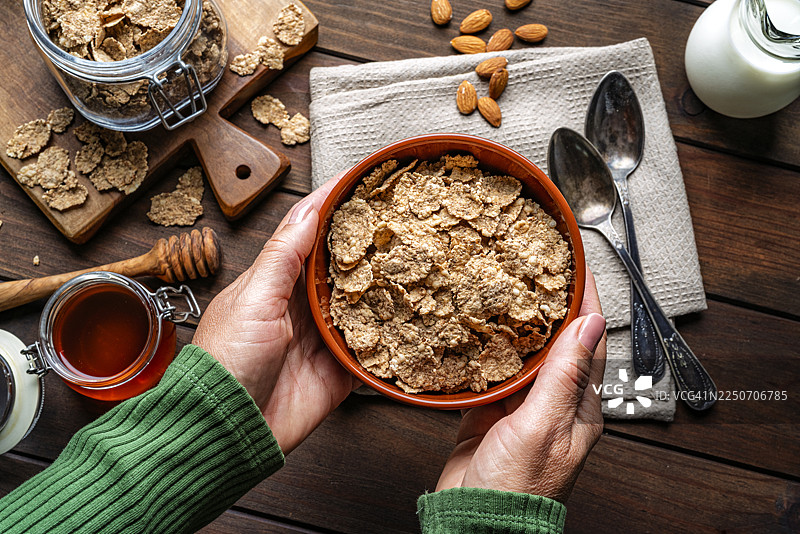 女性的手在乡村风格的木桌上捧着一碗新鲜健康的杂粮麦片。早餐谷物、健康饮食或节食。富含膳食纤维和碳水化合物的食物图片素材