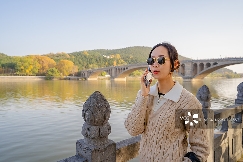 一位女士在风景优美的河边桥上讲电话图片素材