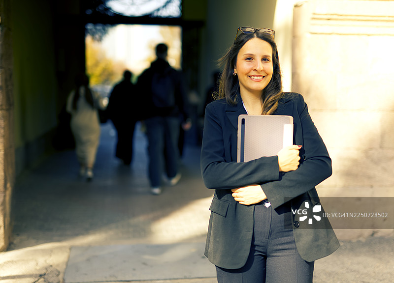 一位女大学生在大学校门口，手持平板电脑，摆出造型。图片素材