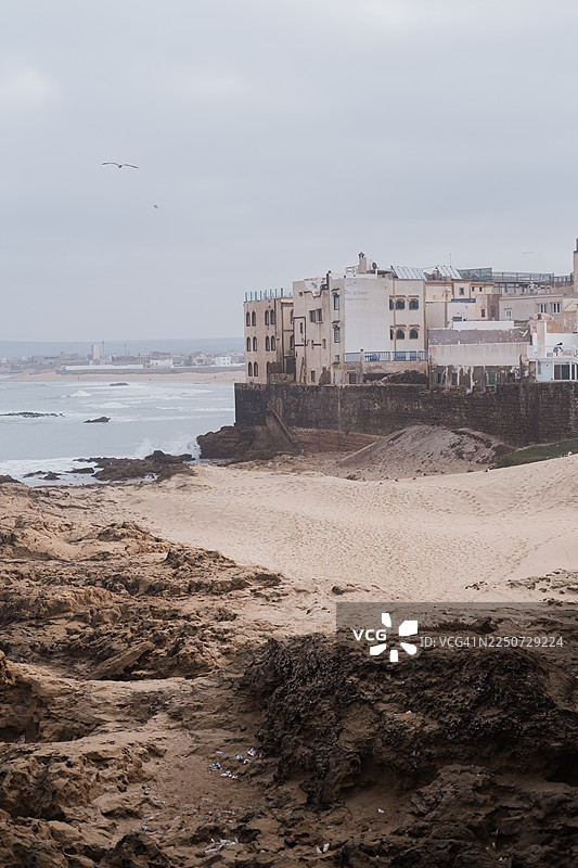 柔和阴沉的海景，展示了坐落在岩石海岸和苍白沙滩上饱经风霜的建筑，营造出一种宁静、忧郁的海岸氛围。图片素材