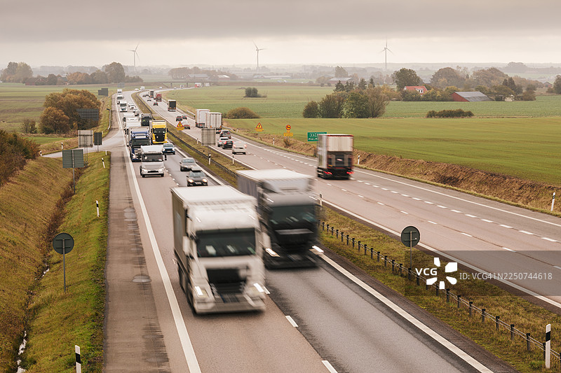 农田景观中的高速公路上行驶的汽车和卡车交通。图片素材